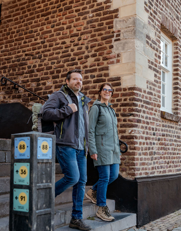 Een koppel in outdoor kleding wandelt een trapje af langs een knooppunt in het centrum van Elsloo