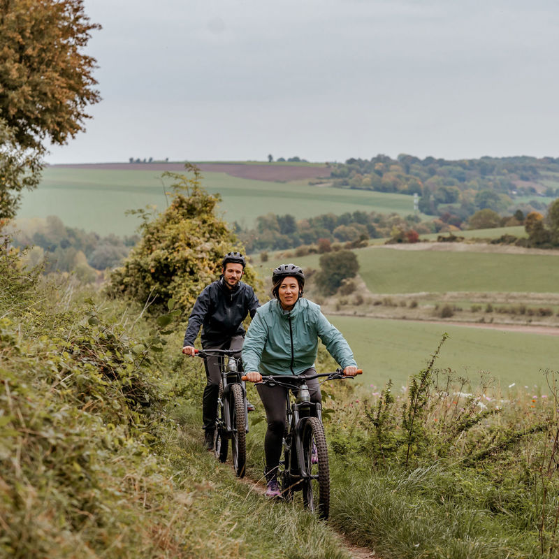 Koppel op mountainbike fietst achter elkaar op een smal pad in het Heuvelland.