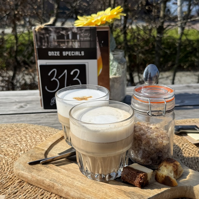 Twee cappuccino's op tafel van een terras in de zon.