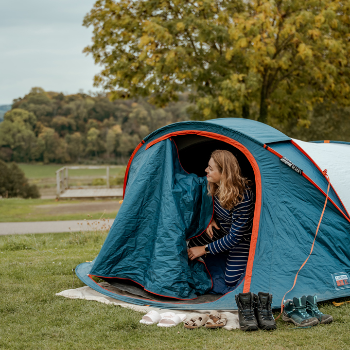 Jonge vrouw opent tent op camping en kijkt naar het heuvellandschap. 