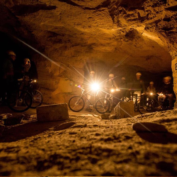Een groep mountainbikers staat in het donker met een lampje klaar om te gaan fietsen in de sibbergroeve grot