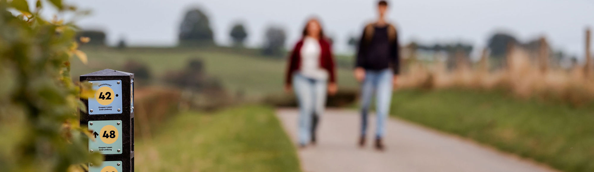 Knooppuntenpaaltje 42 staat langs de weg en twee wandelaars die wazig zijn gemaakt lopen richting het paaltje