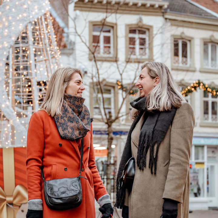Twee vriendinnen in winterse outfit in gezellig met kerstversiering verlichte winkelstraat.