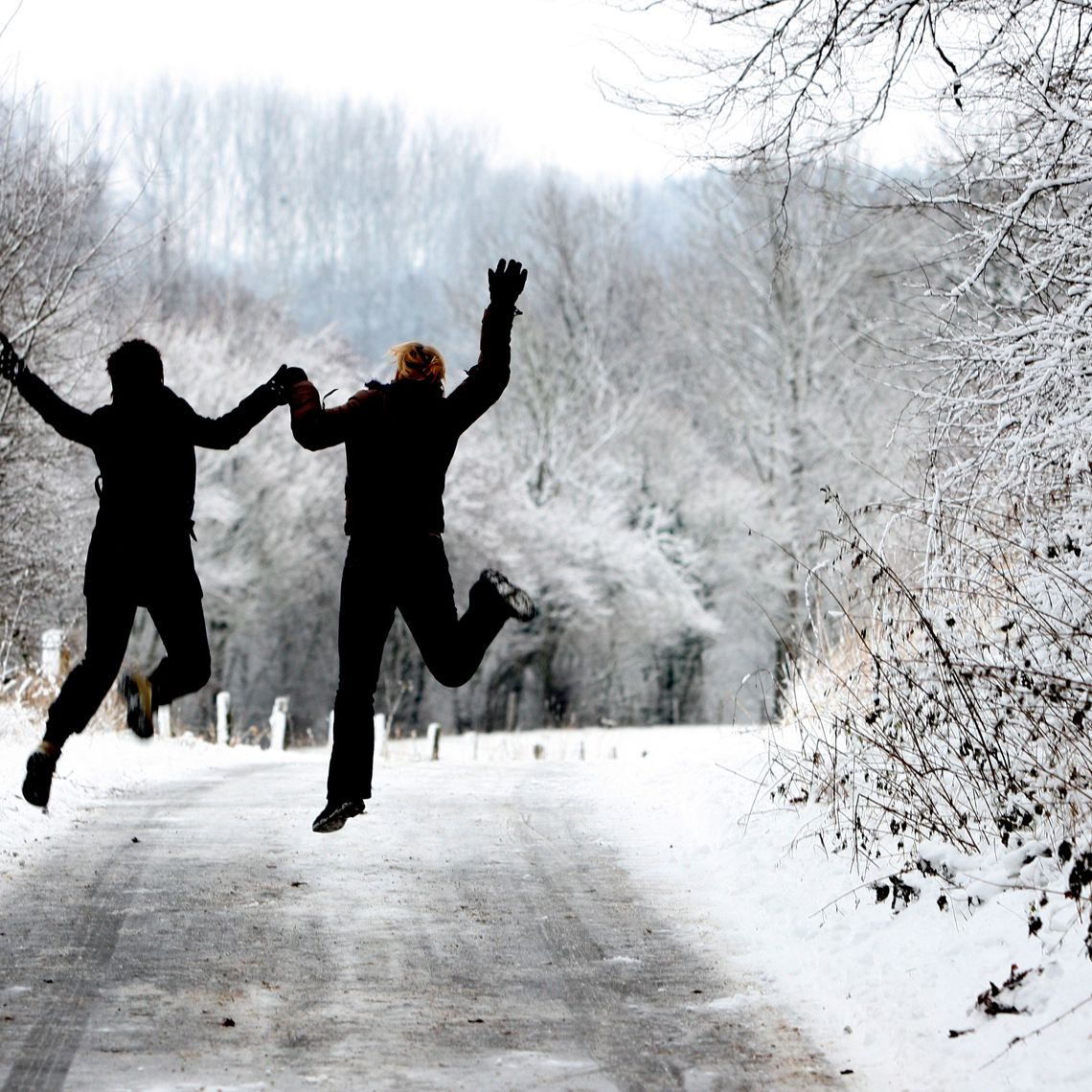 Twee mensen springend in de lucht in besneeuwd bos