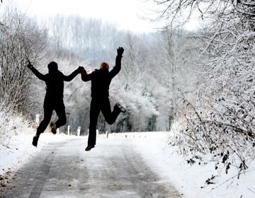 Twee mensen springend in de lucht in besneeuwd bos