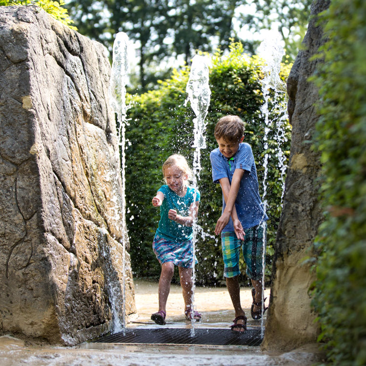 Kinderen rennen door fontein bij het Drielandenpunt doolhof