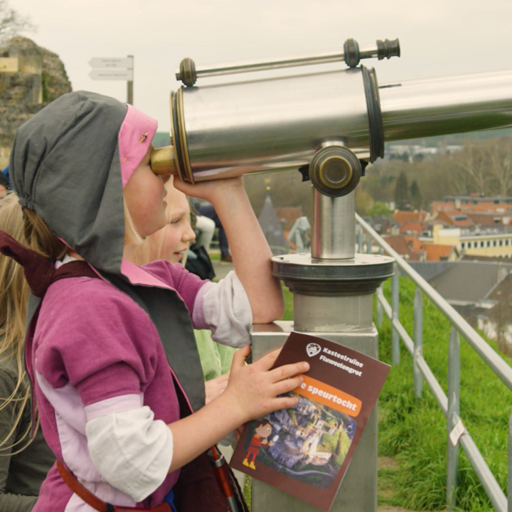 Verkleed kind kijkt door vaste verrekijker bovenop kasteelruine Valkenburg