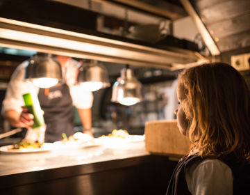 Kind staat in de keuken van een restaurant en bekijkt hoe de koks het eten bereiden