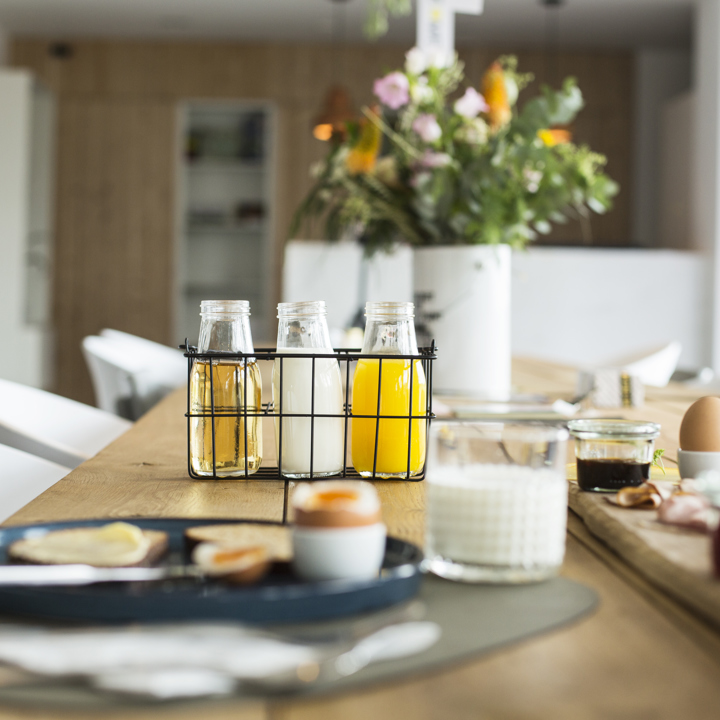 Gedekte ontbijttafel met vers sap, een eitje, glas melk en een houten plank met smeersels.