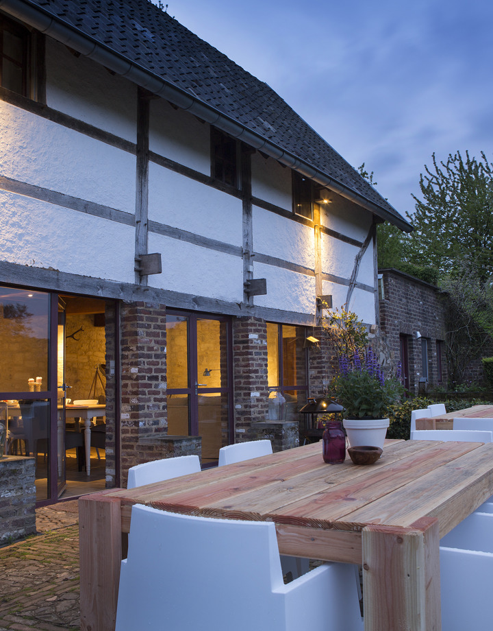Terras met tafels en stoelen naast een karakteristieke boerderij tijdens schemering