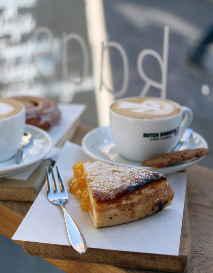 Close up van houten plankje met daarop een stuk abrikozenvlaai en een cappuccino
