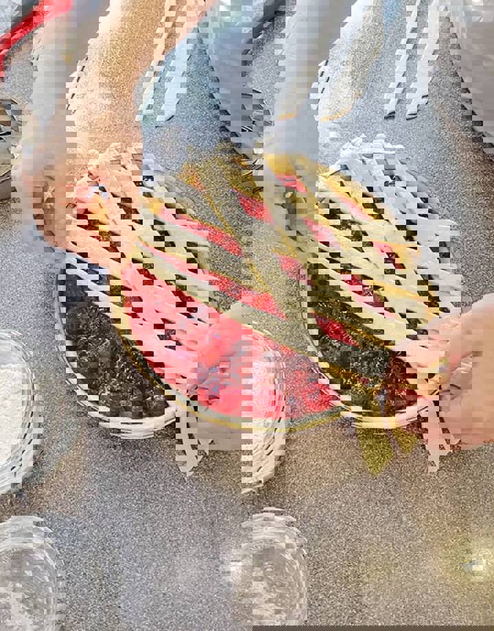 Iemand vlecht deeg over een aardbeienvlaai