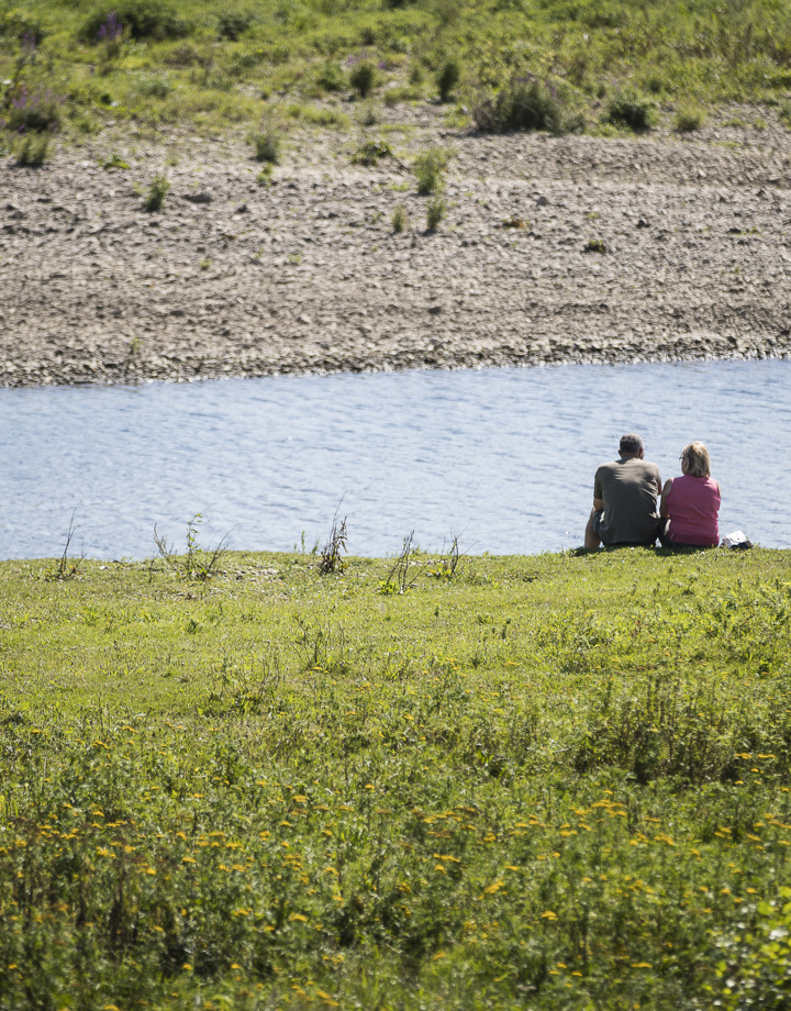 Een koppel zit op het grasveld naast de Maas