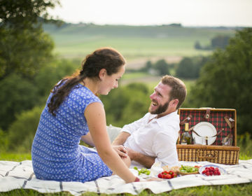 Man en vrouw genieten op weide van een picknick met achterliggend heuvellandschap