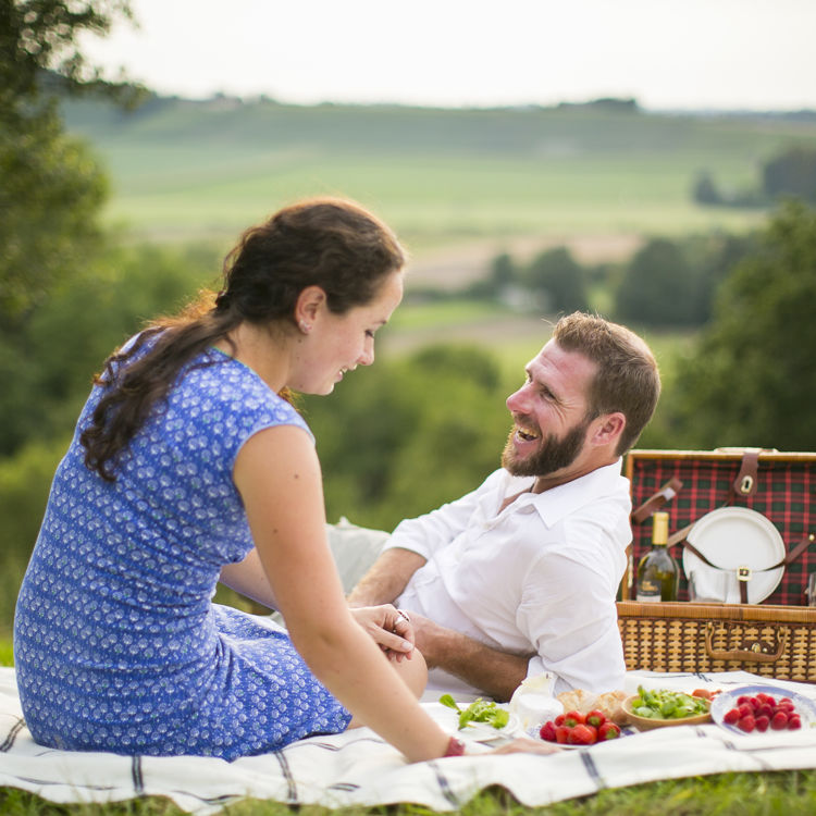 Man en vrouw genieten op weide van een picknick met achterliggend heuvellandschap