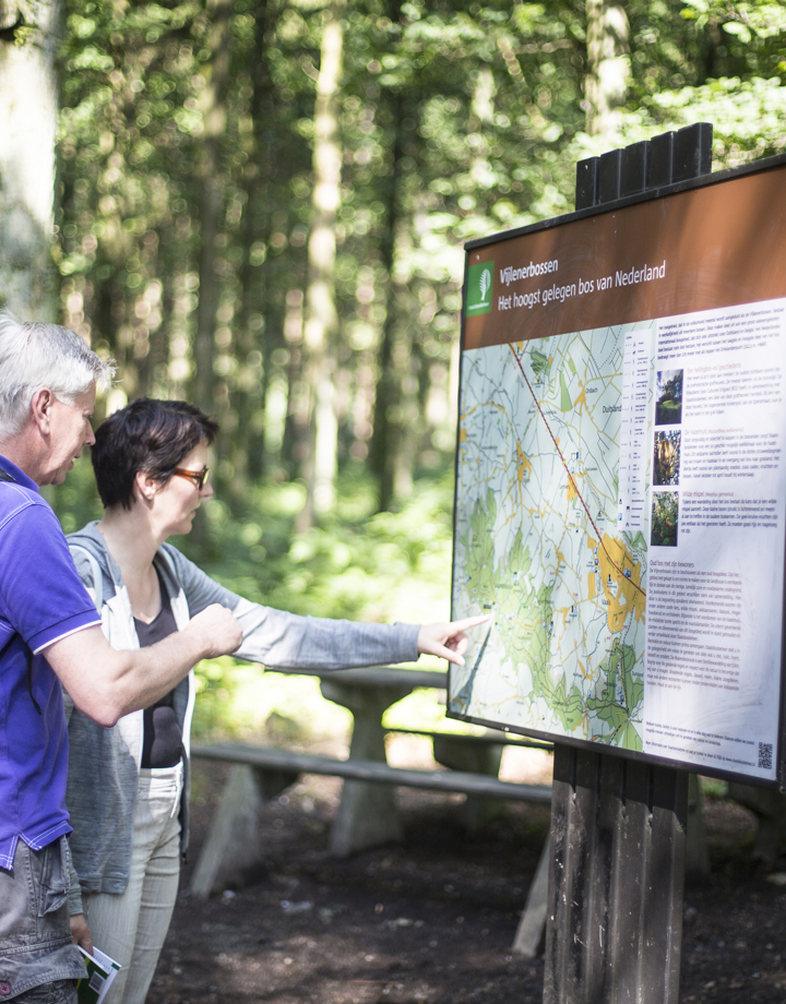Twee wandelaars kijken op een infobord voor wandelroutes in het Vijlenerbos