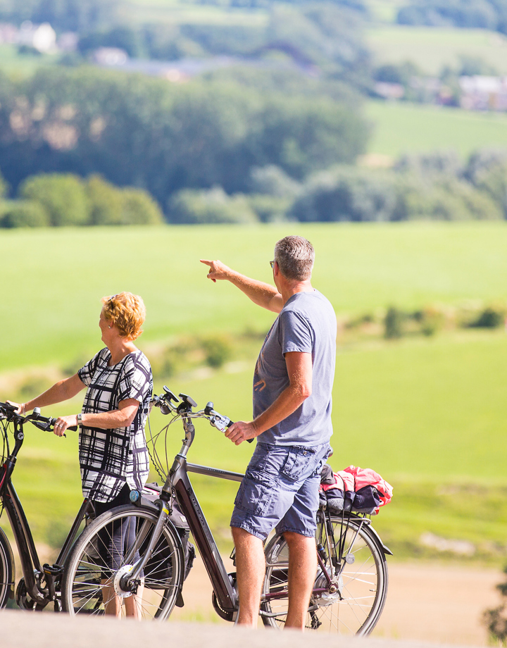 Twee personen met twee fietsen wijzend naar het heuvelland in de zomer