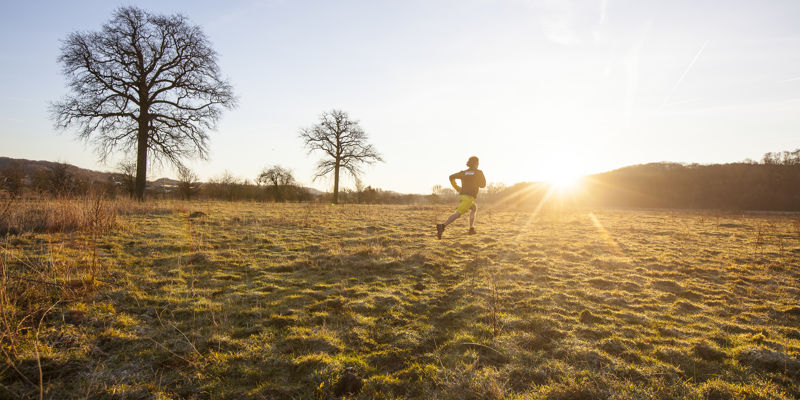 Een mannelijke jogger loopt hard over de heide met een laagstaand zonnetje op de achtergrond