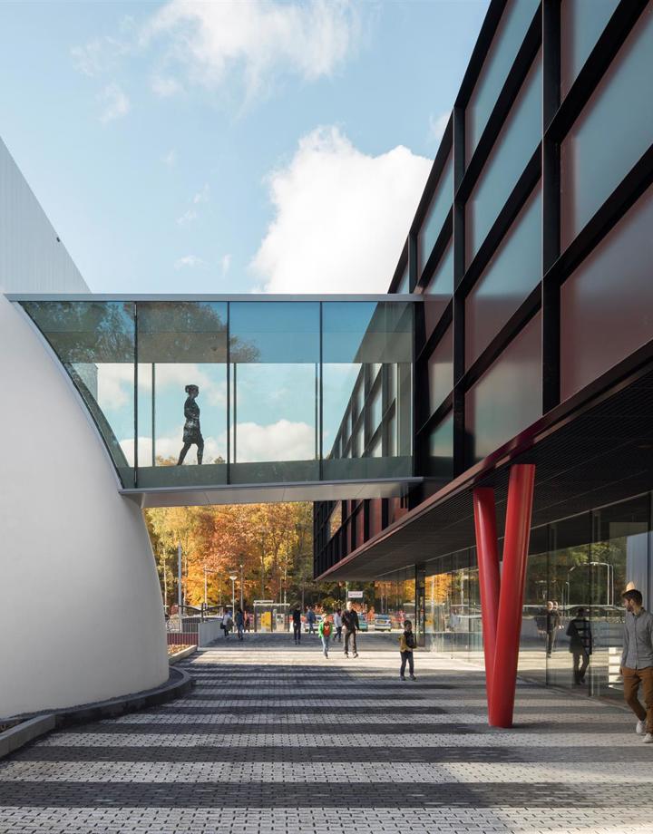Persoon in glazen tunnel die twee moderne gebouwen met elkaar verbindt