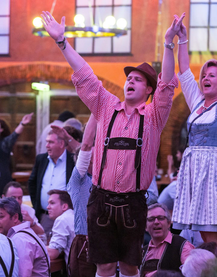 Man en vrouw in tiroolse outfit staan op bank met handen in de lucht tijdens Oktoberfest in Sittard