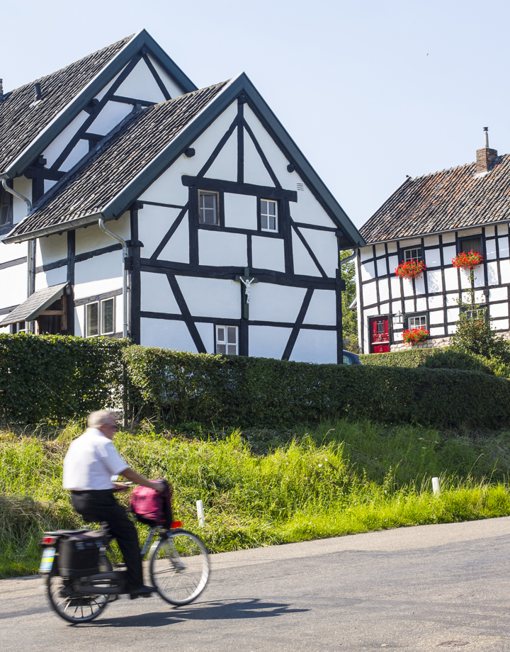 Een oude man fietst langs twee vakwerkhuizen