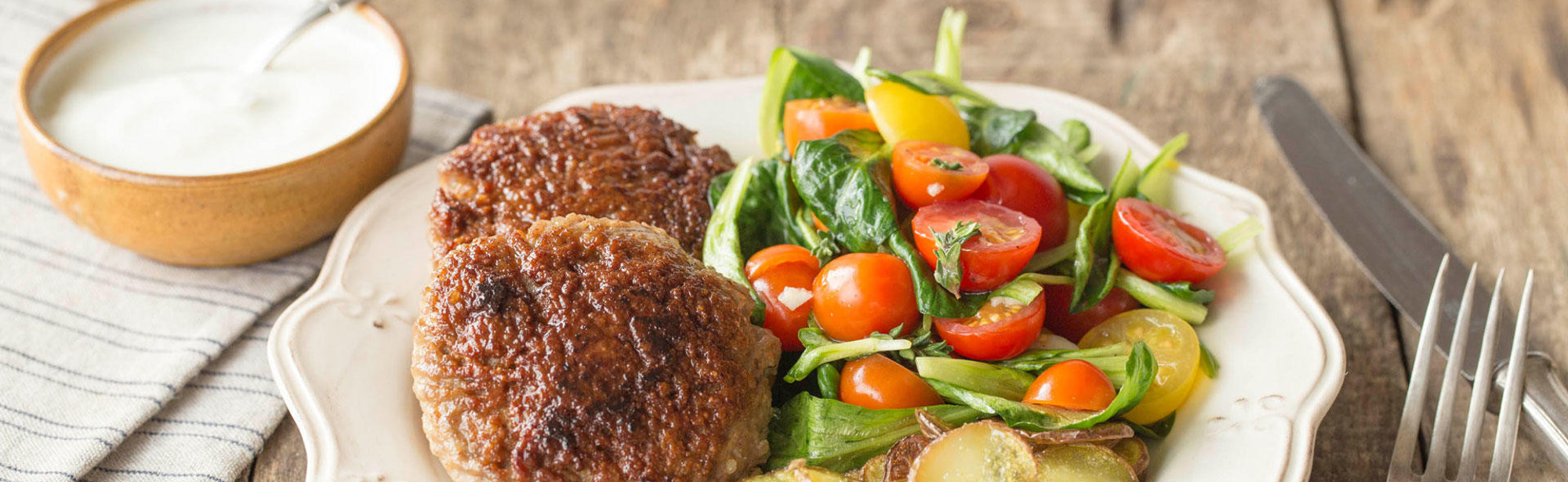 Livar lende gehaktballen geserveerd op een bord met aardappeltjes en salade met tomaten en een bakje saus