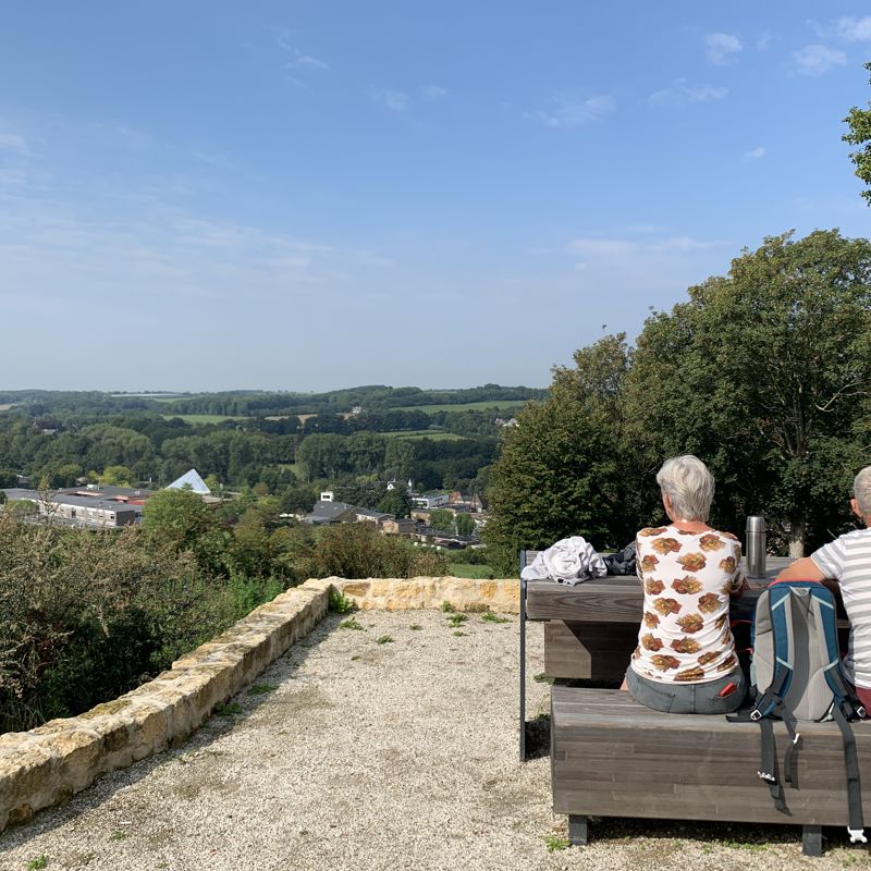 Twee mensen picknicken in het zonnetje aan een tafel met uitzicht over de heuvels