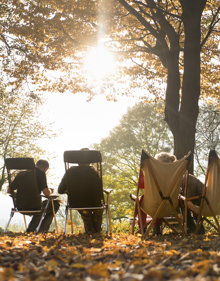 Groep zit op kampeerstoeltjes te genieten van de zon tussen de herfstbladeren
