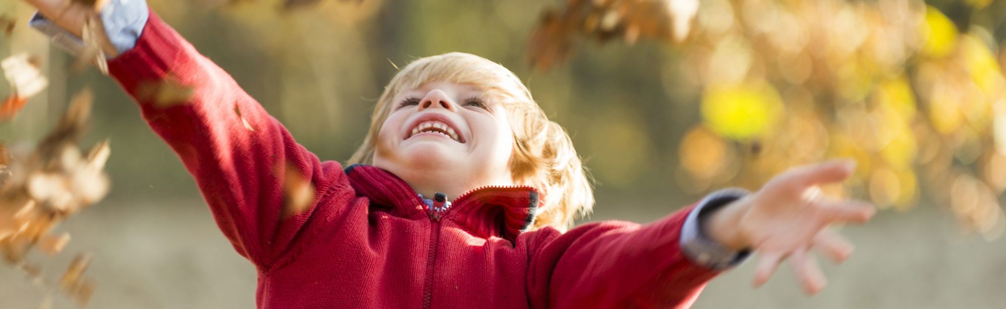 Een jongetje gooit herfstbladeren in de lucht