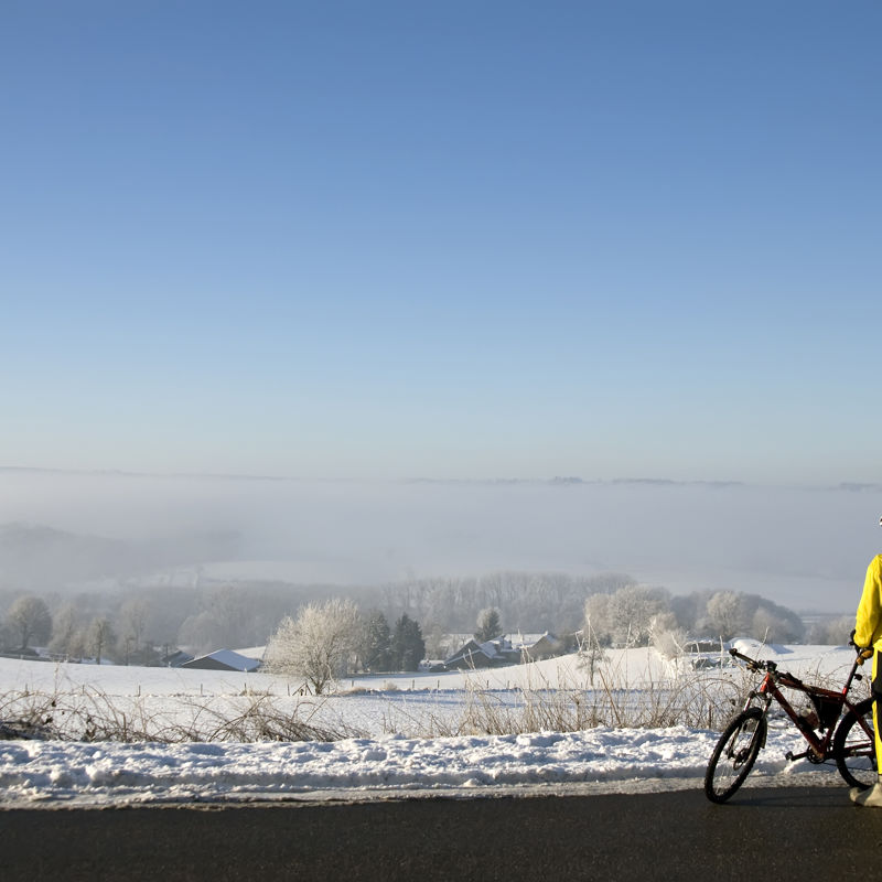 Een MTB'er kijkt uit over een besneeuwd landschap terwijl hij naast zijn fiets staat