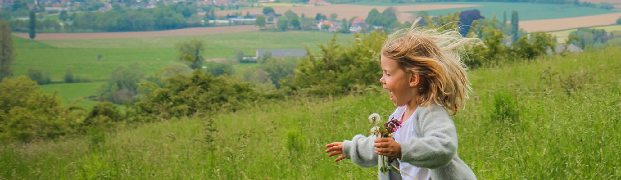 Meisje met geplukte bloemetjes in haar hand rent door het Heuvellandschap