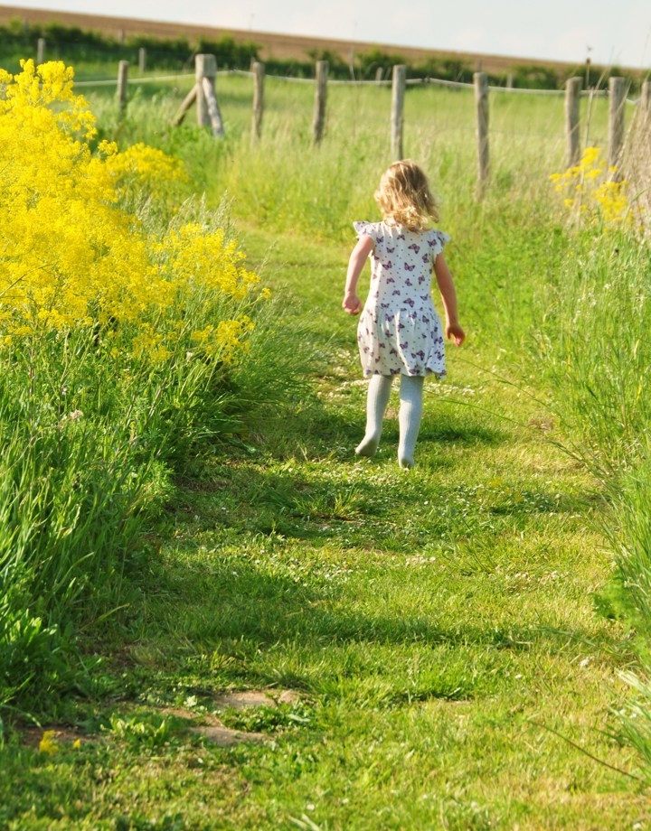Meisje met vlinderjurk loopt door het gras langs gele bloemen