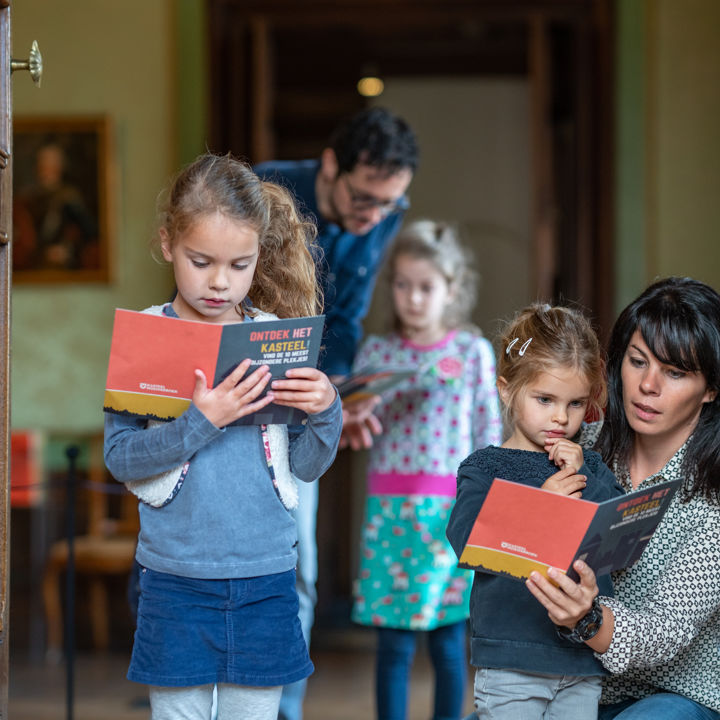 Kinderen lezen aandachtig in een boekje samen met de ouders in Kasteel Hoensbroek