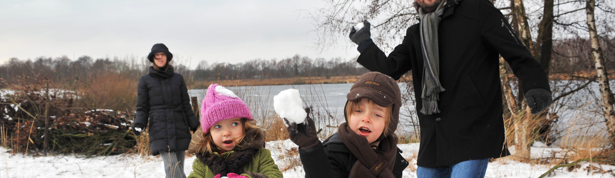 Ouders met twee kinderen gooien met sneeuwballen richting de camera