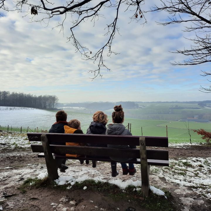 Vier kindjes zitten op een bankje en kijken uit op een winters landschap bij het Gulpdal