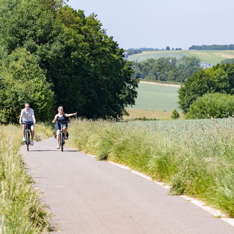 Een koppel fietst door het groene heuvellandschap en de vrouw wijst naar iets in de verte