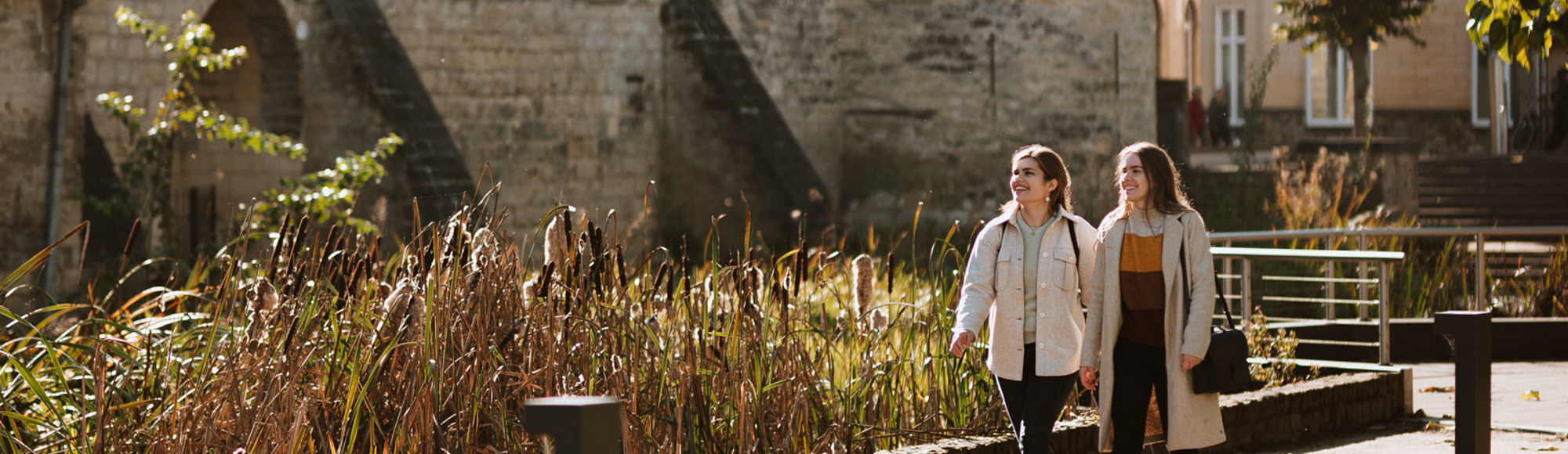 Twee dames lopen door een parkje in Valkenburg met op de achtergrond gebouwen van mergel en steen