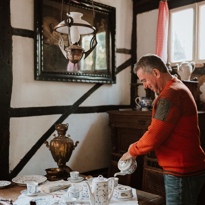 Een meneer schenkt een kopje koffie in een oud Limburgs servies binnen in een vakwerkhuisje