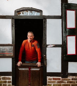Een man kijkt door een oude deurpost vanuit het vakwerkhuis naar buiten