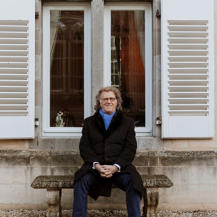 André Rieu poseert op een bankje voor een groot raam met witte luiken