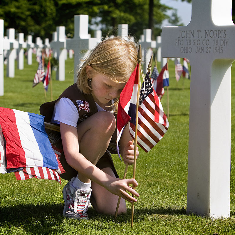 Een meisje plaats een Amerikaanse vlag bij een gedenkkruis op de begraafplaats in Margraten