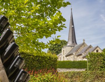 De kerk van Holset met op de voorgrond een stellage van flessen wijn van Domein Holset