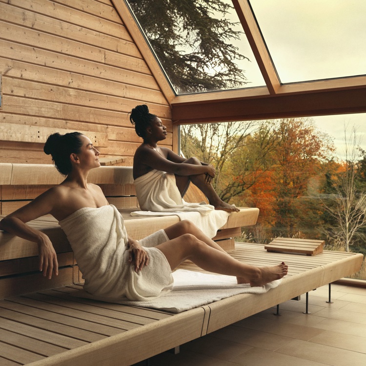 Twee dames ontspannen in de panoramasauna met uitzicht over de herfstige kleuren van de natuur.