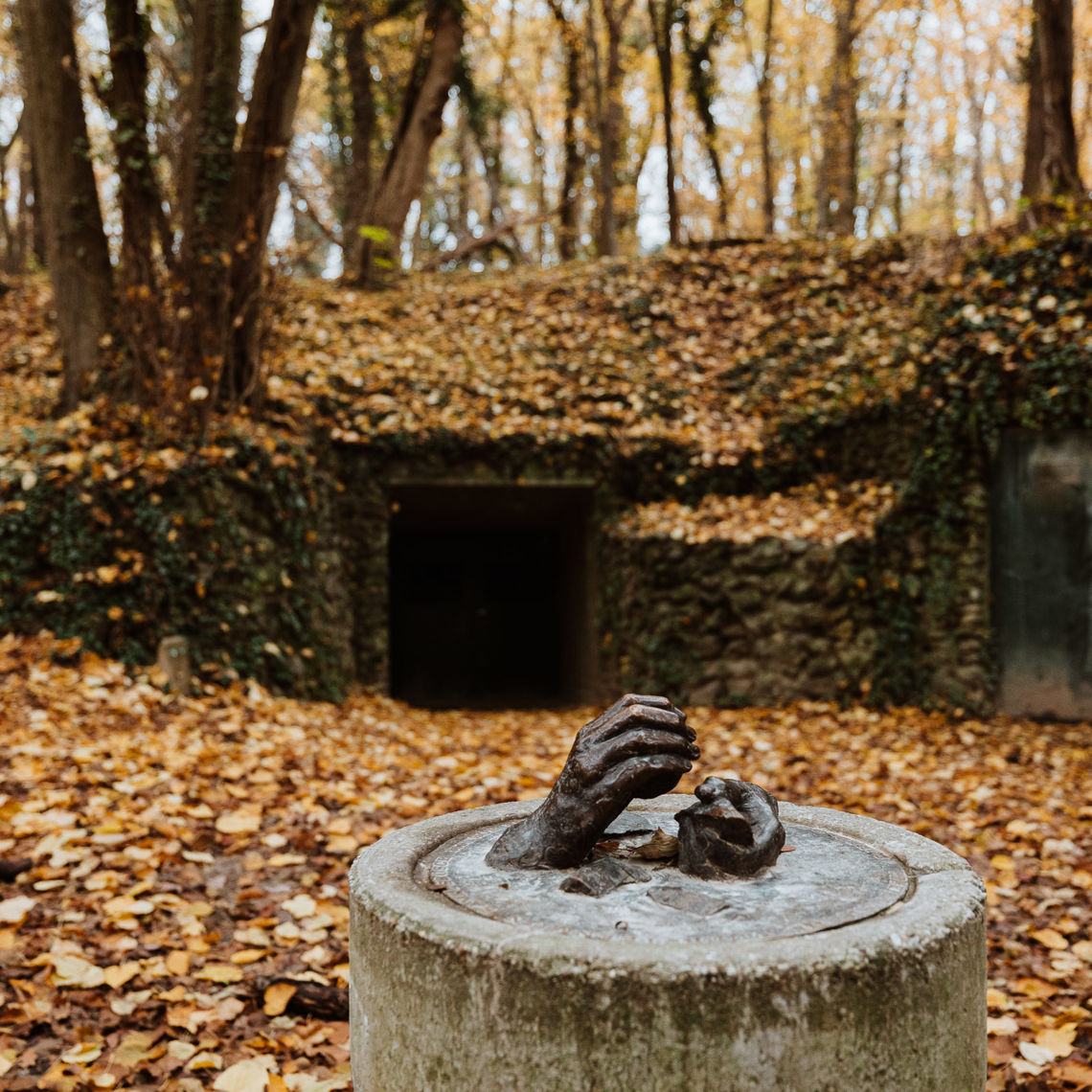 Een beeldhouwwerk met twee handen die vuursteen vasthouden in het bos voor de ingang van de vuursteenmijn 