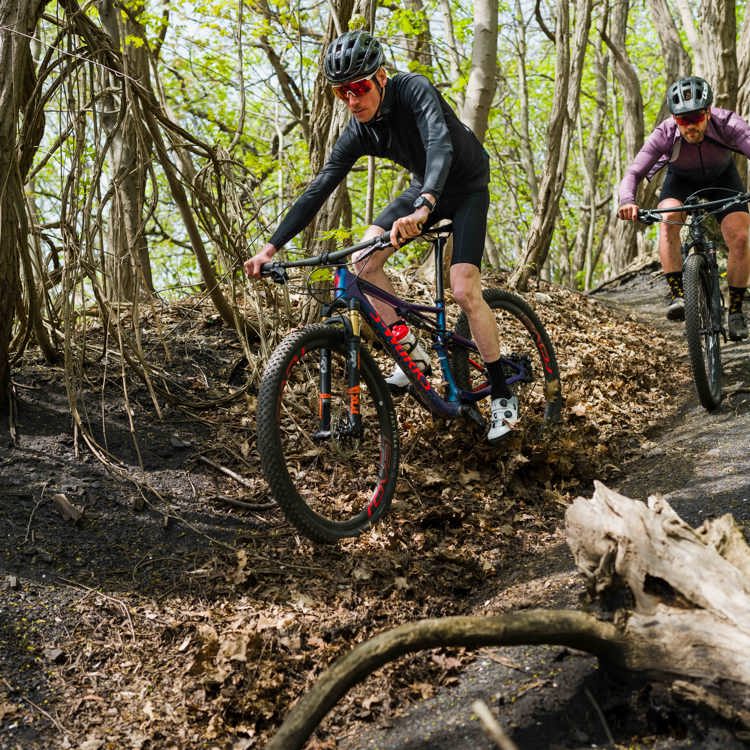 Twee mountainbikers dalen van een smal paadje af in het bos
