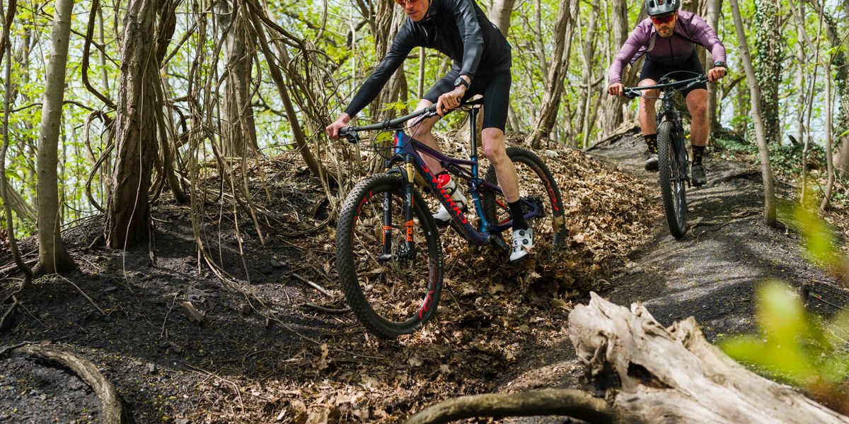 Twee mountainbikers dalen af op een smal paadje in het bos in Zuid-Limburg