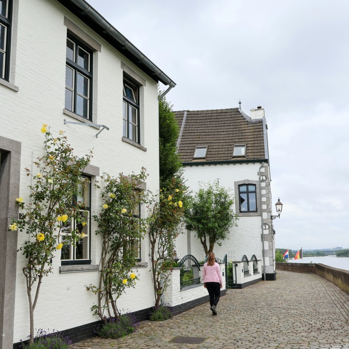 Dame wandelt langs de kade in Eijsden met mooie witte huizen.