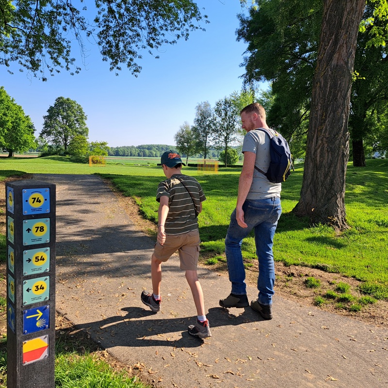Vader met zoontje lopen op een wandelpad naast een knooppunten paaltje.