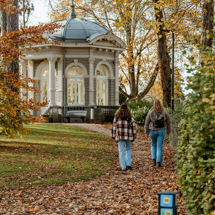 Twee vriendinnen wandelen door het Proosdijpark in Meerssen, over een dek van herfstbladeren.