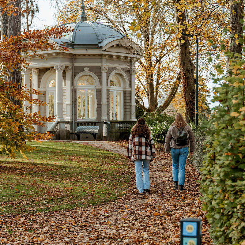 Twee vriendinnen wandelen door het Proosdijpark in Meerssen, over een dek van herfstbladeren.